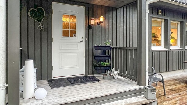 A wooden porch with a white door, a black shelf with plants, and a white statue. - Cozy home in Flekkefjord with house sea view (Flekkefjord)