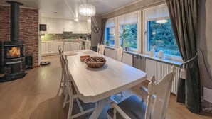 A dining area with a white table and chairs, a stone fireplace, and a view of greenery through large windows. - Cozy home in Flekkefjord with house sea view (Flekkefjord)