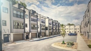 A row of modern apartment buildings with multiple garage doors, a small tree, and a parking area.