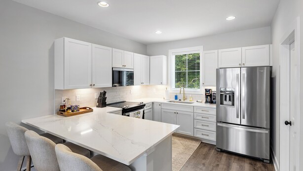 A modern kitchen with white cabinetry, a stainless steel refrigerator, and a marble island with bar stools.