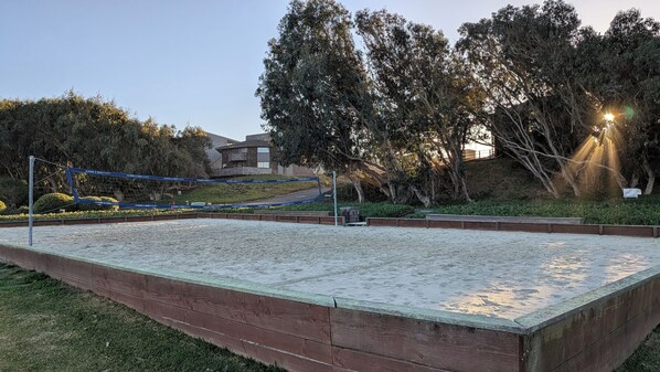 Una cancha de voleibol con red, rodeada por una valla de madera y follaje.