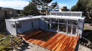Ein Haus am Meer mit einer Holzterrasse, großen Fenstern und Blick auf den Strand.