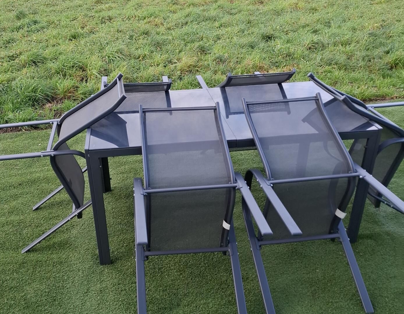 Een set buiten tafels en stoelen van metaal en glas, geplaatst op een grasveld.