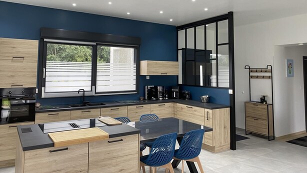 A modern kitchen with a central island, blue chairs, and a large window with blinds. - GITE DE L'ETOILE - ROCROI (ROCROI)
