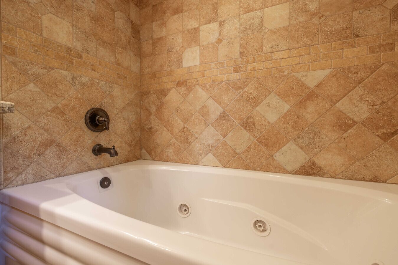 A bathroom with a white bathtub, a shower, and a tiled wall with a diamond pattern.