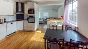 A modern kitchen with white cabinets, a built-in oven, and a dining area with a wooden table and chairs. - 4 bedroom beautiful home in åstorp (Åstorp)