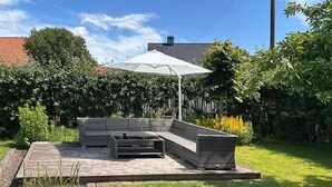 A patio with a sectional sofa and a table, surrounded by a garden and a white umbrella. - 4 bedroom beautiful home in åstorp (Åstorp)