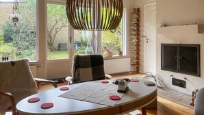 A cozy living room with a round table, chairs, a hanging light fixture, a fireplace, and a view of the garden through the window. - Stunning home in Höllviken with WiFi (Höllviken)
