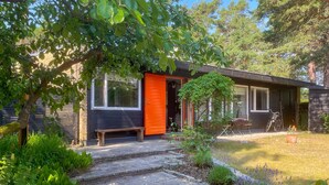 A modern house with a black exterior, an orange door, and a wooden bench outside. - Stunning home in Höllviken with WiFi (Höllviken)