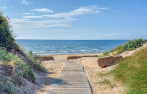A wooden boardwalk leading to a sandy beach with a view of the ocean.