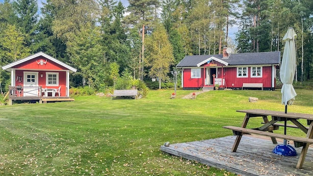 A red cabin with a porch and a deck, surrounded by a grassy yard and trees.