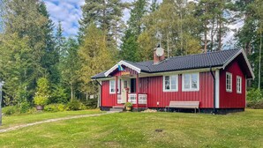A red wooden cabin with a porch, surrounded by a forest.