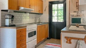 A kitchen with wooden cabinets, a stove, a microwave, and a window with a view of greenery.