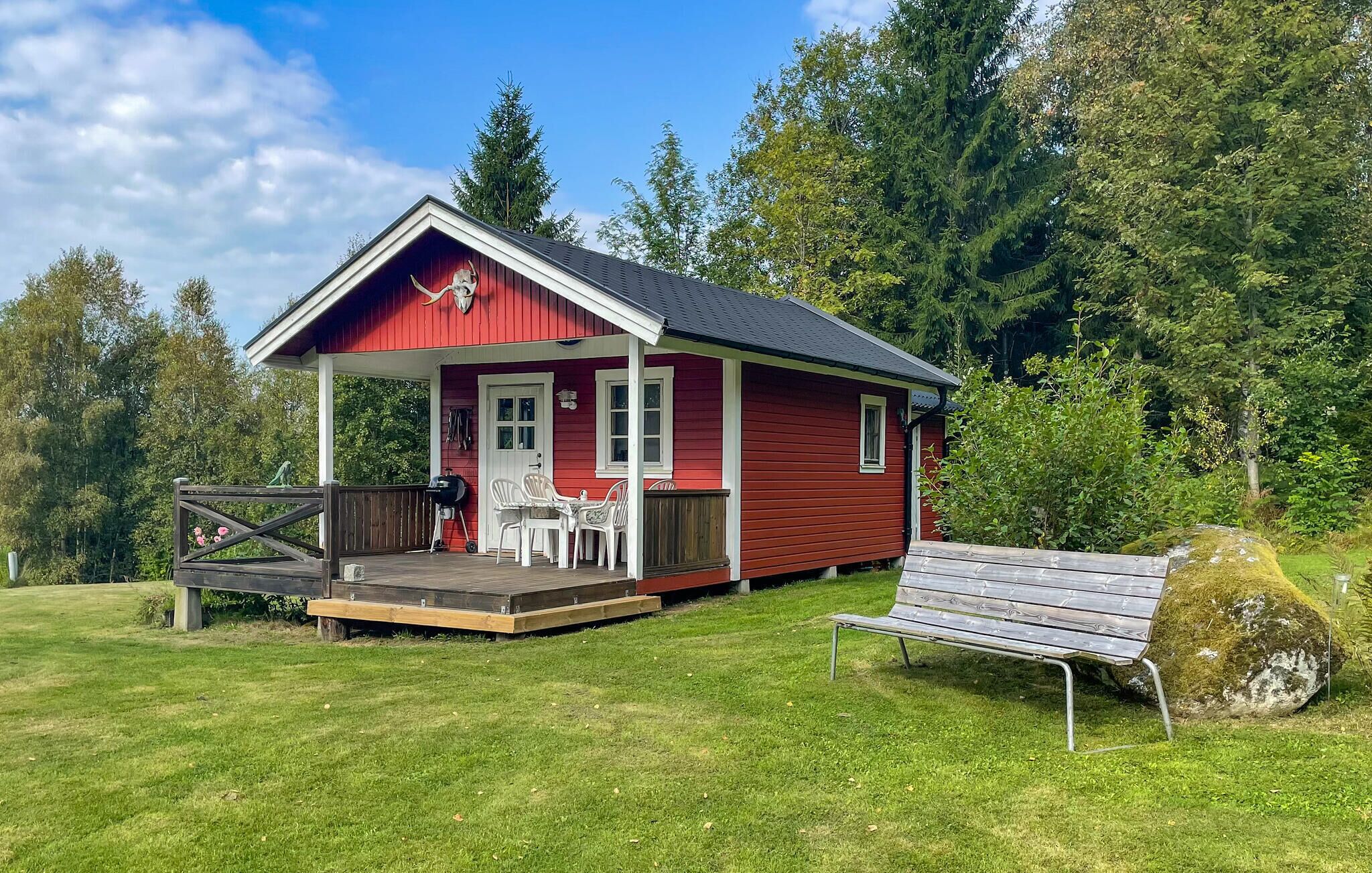 A red cabin with a porch, a table, and chairs, surrounded by a grassy area and trees.