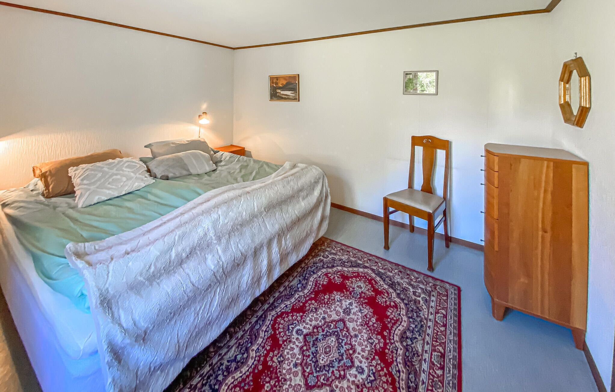 Een slaapkamer met een bed, een stoel, een houten kast en een vloerkleed.