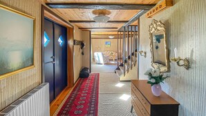Un couloir avec un plafond en bois, une moquette rouge à motifs, une commode en bois ornée d’un vase de fleurs et un grand miroir avec un cadre travaillé.