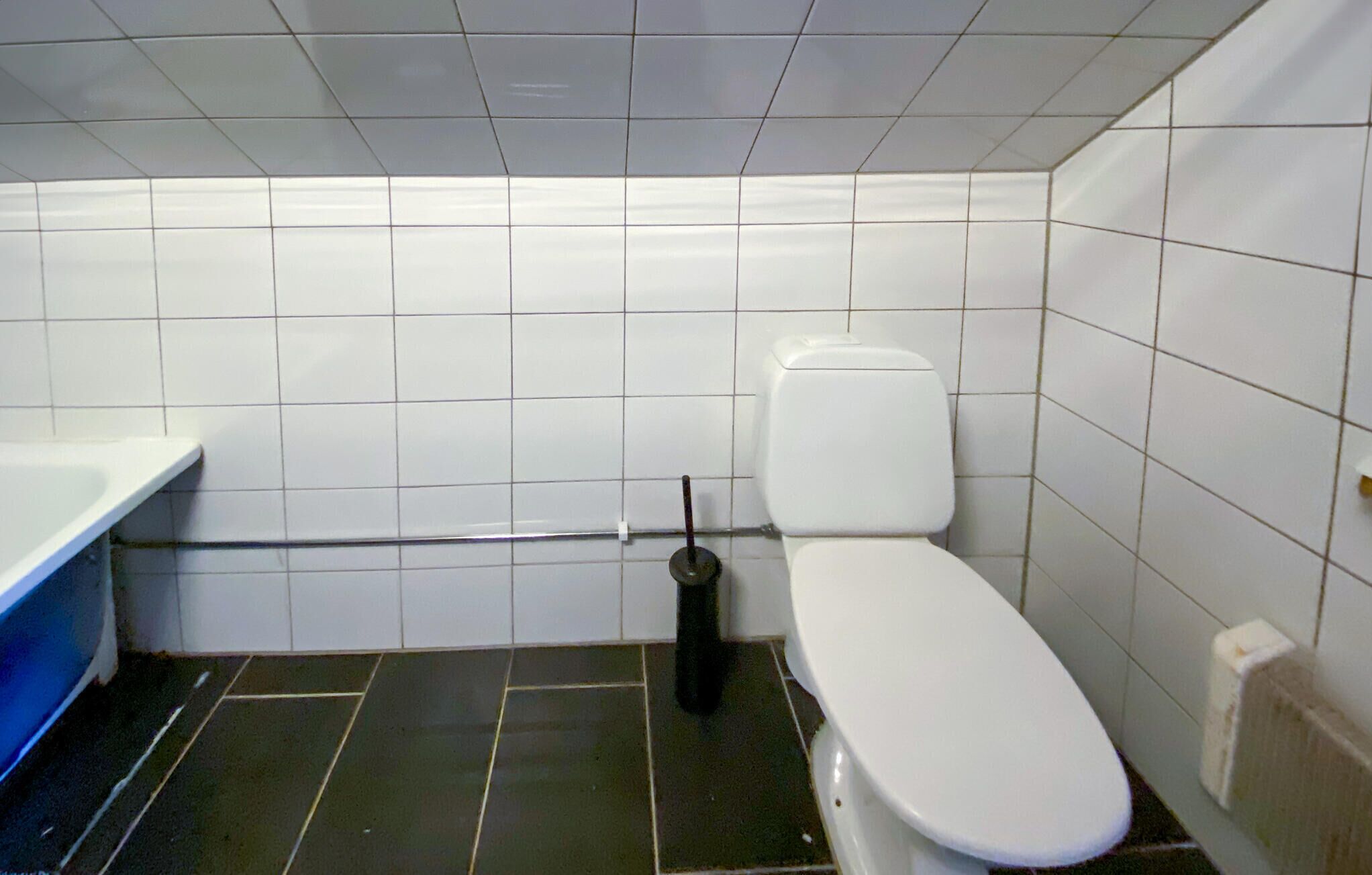 Un baño pequeño con azulejos, un inodoro blanco, piso negro y un lavamanos blanco.