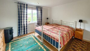 Een slaapkamer met een bed, nachtkastje, lamp, kledingkast en een raam met gordijnen.