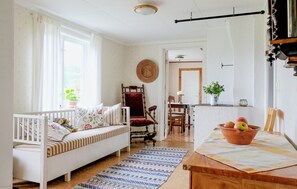 A cozy living room with a white sofa, a red chair, a dining table with a bowl of fruit, and a view of a garden through the window. - 2 bedroom awesome home in Flisby (Flisby)