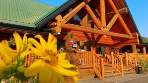Une cabane en rondins avec un toit végétalisé, un revêtement extérieur en bois et une statue d’ours sur le porche.