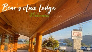 Un chalet en bois doté d’un porche couvert, d’une enseigne en pierre et offrant une vue sur la route et les montagnes.