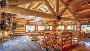 Un intérieur de style chalet, avec des poutres en bois, une cheminée en pierre et plusieurs coins salon.