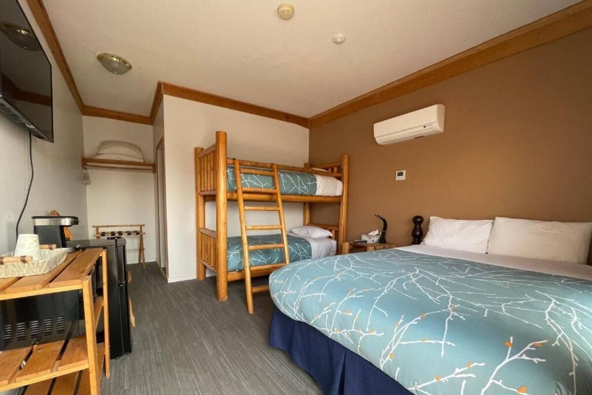 A room with bunk beds, a desk with a computer, a chair, a bed with a blue and white patterned bedspread, and an air conditioning unit on the wall.
