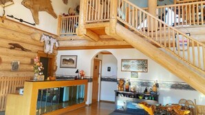 Un hall d’entrée spacieux avec un comptoir de réception en bois, un escalier et divers éléments de décoration murale, notamment des peaux d’animaux et un tableau.
