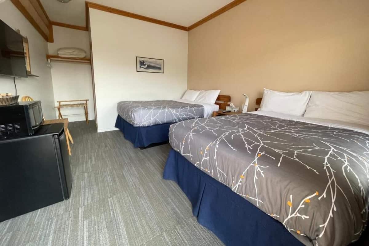 A hotel room with two beds, a desk, a chair, and a microwave.