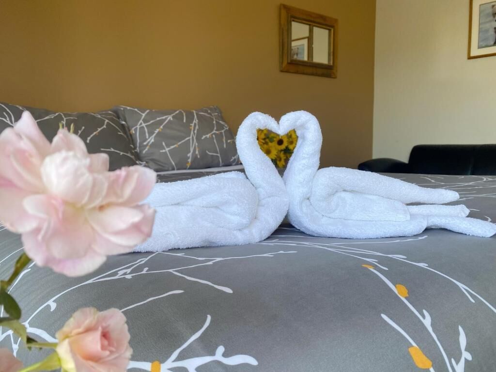 Un lit recouvert d’une couvre-lit à motifs gris et blancs, une disposition de serviettes en forme de cœur et une fleur rose au premier plan.