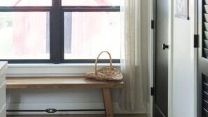 Un pasillo con un banco, una ventana que da a un edificio rojo y una puerta con picaporte negro.
