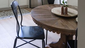 Una cocina moderna con armarios blancos, un refrigerador de acero inoxidable, una mesa de comedor de madera con sillas y una lámpara decorativa.
