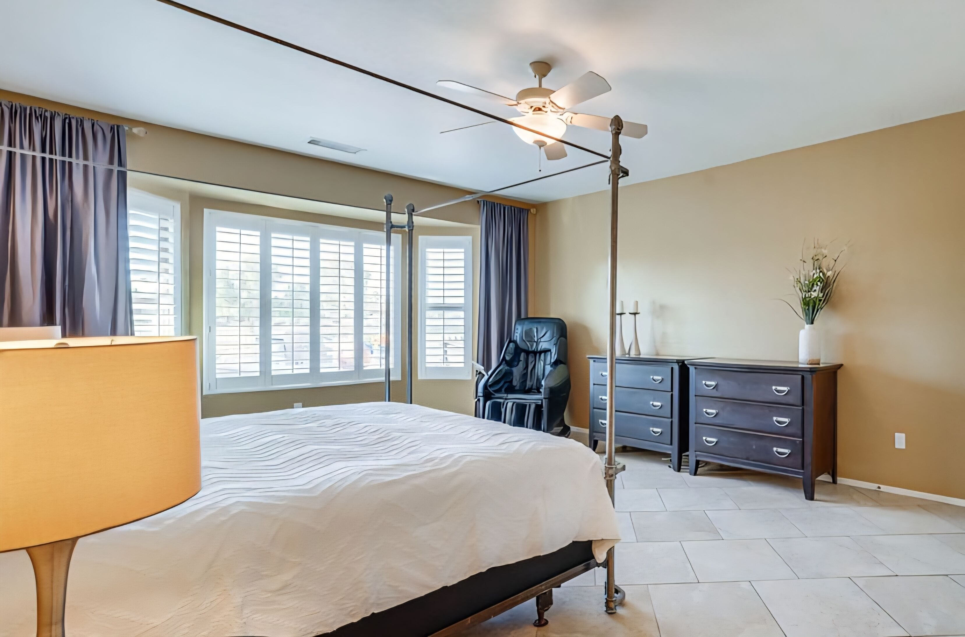 A bedroom with a bed, a desk, a chair, a dresser, and a ceiling fan.