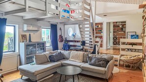 Un saló modern amb un sofà modular, una taula rodona petita, una guitarra i una escala que condueix a un nivell superior.