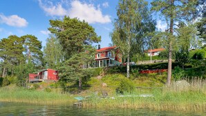 A lakeside cabin with a red exterior, a glass-enclosed porch, and a wooden deck. - Pet friendly home in Vätö with sauna (Vätö)