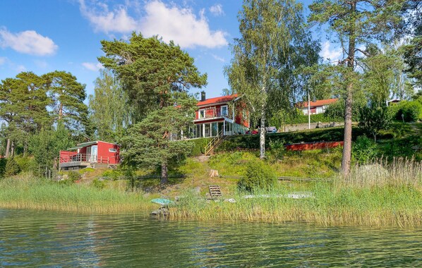 Eine am See gelegene Holzhütte mit roter Fassade, einer gläsernen Veranda und einer Holzterrasse.