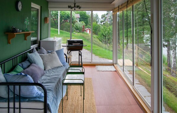 Une pièce chaleureuse avec un mur vert, un canapé agrémenté de coussins à motifs, une petite table et un barbecue à l’extérieur de la fenêtre.