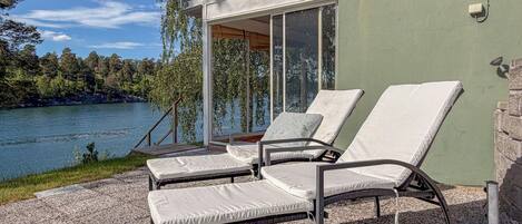 A terrace with two lounge chairs, a table, and a view of a lake and forest.