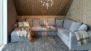 A cozy attic bedroom with a sloped ceiling, a gray sectional sofa, a patterned rug, and a modern chandelier. - Amazing home in Sysslebäck with sauna (Sysslebäck)