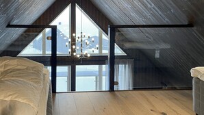 A high-ceilinged attic bedroom with large windows, a chandelier, and wooden flooring. - Amazing home in Sysslebäck with sauna (Sysslebäck)