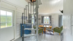 Une pièce dotée d’un escalier en colimaçon, d’une table à manger avec des chaises, et offrant une vue sur l’extérieur grâce à de grandes fenêtres.