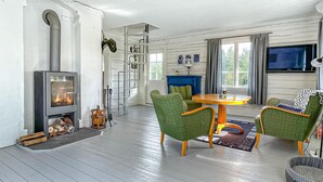 Un salon chaleureux avec une cheminée, des fauteuils à revêtement vert, une table en bois et un téléviseur fixé au mur.