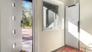 Un pasillo con un ventanal corredera que da a una terraza, una ventana grande con persianas y una puerta blanca con manija.