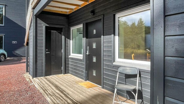 Una casa de madera oscura con un porche, una puerta y una ventana.