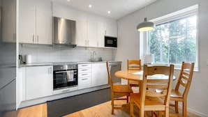 Una cocina moderna con armarios blancos, horno empotrado y zona de comedor con sillas y mesa de madera.