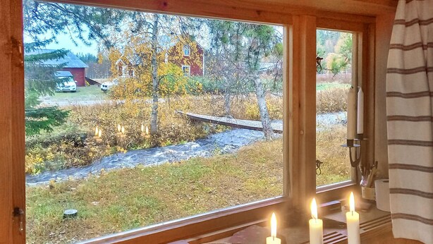 Een kamer met een groot raam dat uitkijkt op een landelijk landschap met herfstbomen en een houten brug.