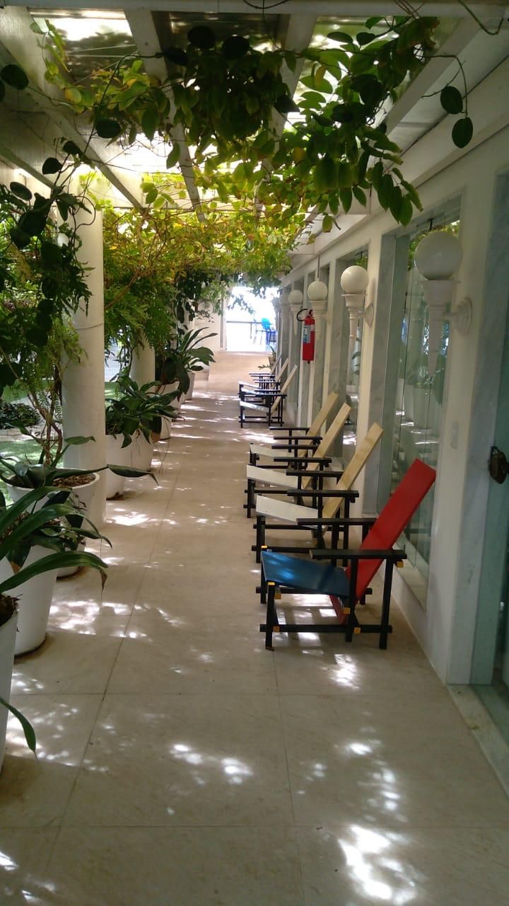 A corridor with potted plants on the left, benches on the right, and a tiled floor.