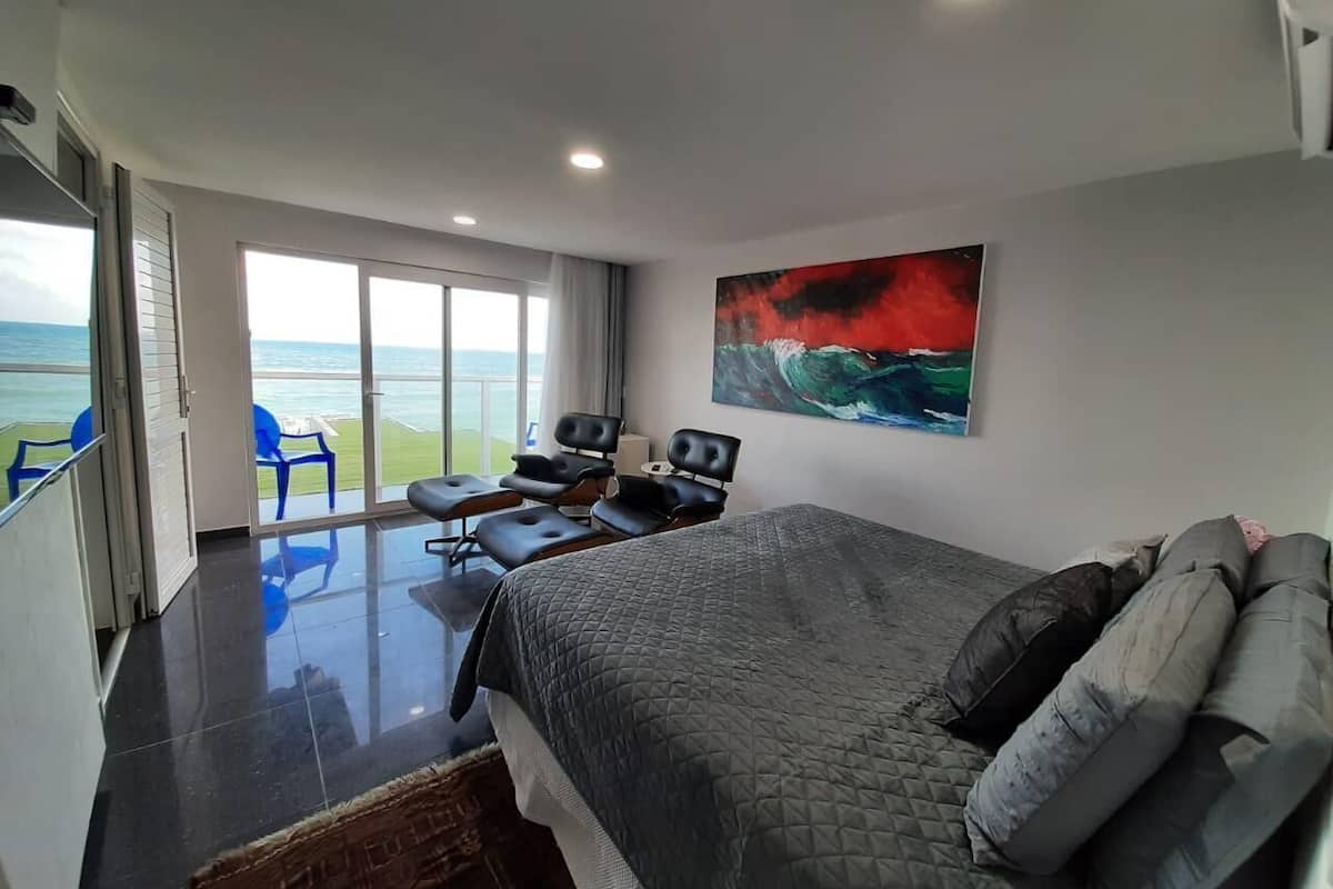 Un dormitorio moderno con una cama grande, vistas al océano y un balcón con sillas.
