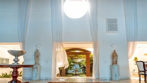 A spacious room with a large patterned rug, a round ceiling light, and a view of a garden through an open doorway. - Vila Mar Hotel (Olinda)