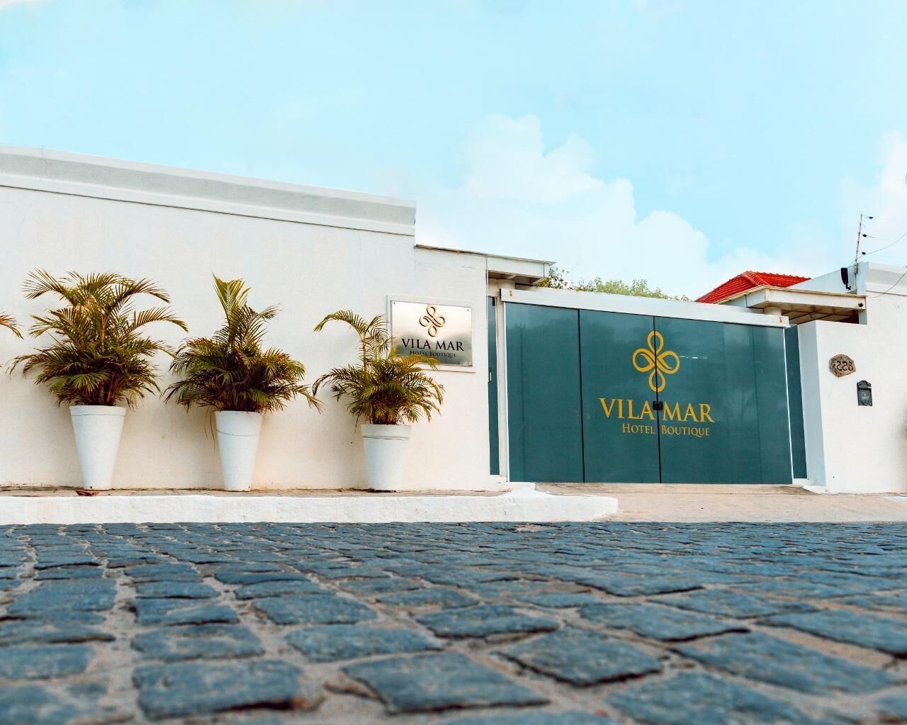 Un edificio con un portón de entrada verde, con la leyenda "Vila Mar Hotel Boutique", y tres plantas en macetas al frente.